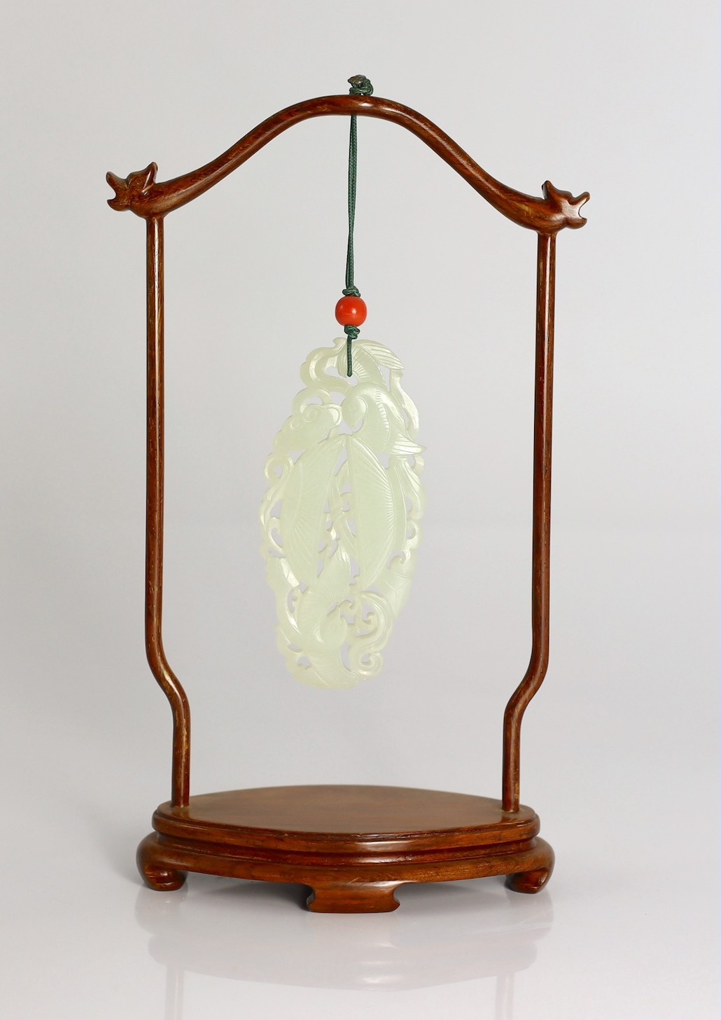 A Chinese white jade twin phoenix reticulated plaque, 19th century, 8.7cm, suspended from a wood stand with coral bead to the cord